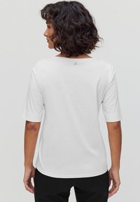 Vit kortärmad topp med en avslappnad passform. Har en rund halsringning med en liten ögla baktill. Slätt bomullstyg.