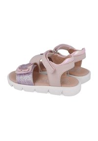 Sandalias de cuero rosa con un acento de flor, una correa brillante, diseño abierto y una suela blanca texturizada. Cierre en el tobillo ajustable.