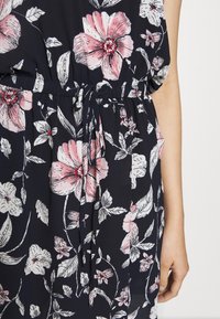 Robe fleurie en tissu bleu marine avec de grandes fleurs roses et blanches, taille cintrée avec cordon de serrage et manches courtes.