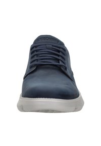 Zapatilla azul marino hecha de material sintético suave, con punta redonda, diseño de cordones y suela de goma blanca con patrones de tracción.