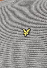 Gråt striped stof med ribbet tekstur, med en lille gul og sort broderet ørnelogo på venstre side.