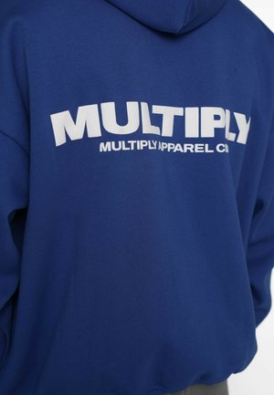 Hanorac albastru cu glugă, având pe spate un logo alb mare „MULTIPLY”, realizat dintr-un material moale, cu croială lejeră și mâneci lungi.