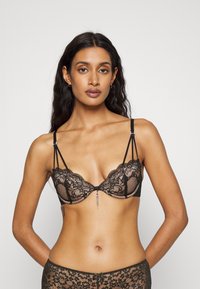 Zwarte kanten bh met onderwire, semi-doorzichtige cups, ingewikkelde bloempatronen en verstelbare bandjes. Centraal accent met een hangende kettingdetail.