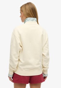 Crèmekleurig sweatshirt met een hoge kraag, geribbelde manchetten en een gelaagd groen gestreept kraagdetail, gecombineerd met rode korte broek.