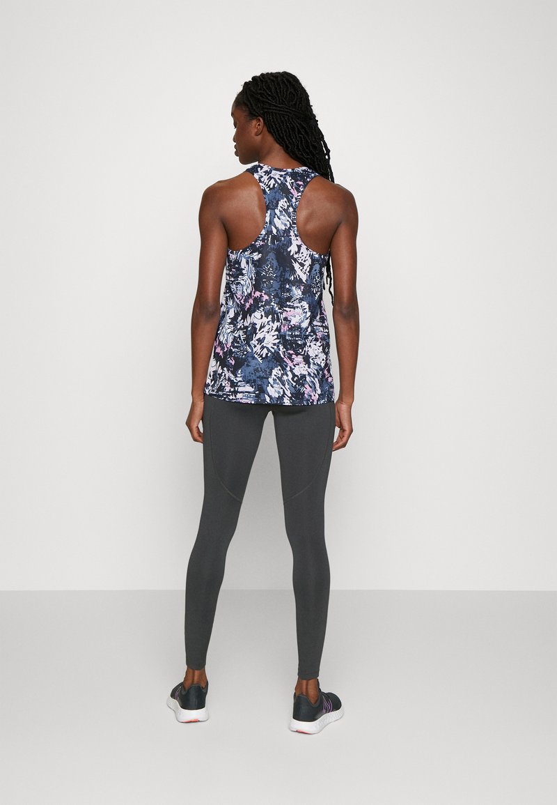 Débardeur à imprimé floral bleu marine, avec un design dos nageur. Assorti avec des leggings gris ajustés, présentant des accents de couture et des chaussures de sport.