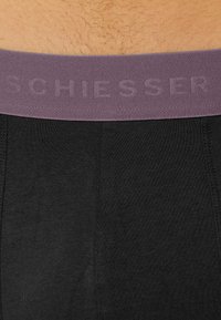 Boxer neri realizzati in un materiale liscio, con una vita larga e strutturata di colore viola, dotata del marchio in rilievo "SCHIESSER."
