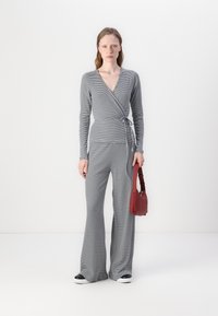 Súprava so šedobielym pruhovaným cape topom a rozšírenými nohavicami, stredne ťažký materiál, doplnená červenou kabelkou a teniskami s čiernymi detailmi.