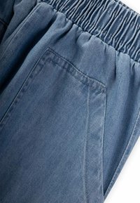 Svijetloplave traperice s elastičnom navlakom. Imaju bočnu džepu i vidljive detalje prošivanja, pokazujući glatku teksturu.