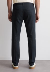 Pantaloni neri dal taglio slim, realizzati in tessuto di cotone liscio, con vita standard e due tasche posteriori dal rifinitura pulita.