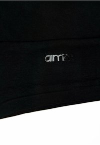 Zwarte stof met een gladde textuur heeft een prominent zilveren logo "aimn" dicht bij de rand, wat een strakke en minimalistische uitstraling laat zien.