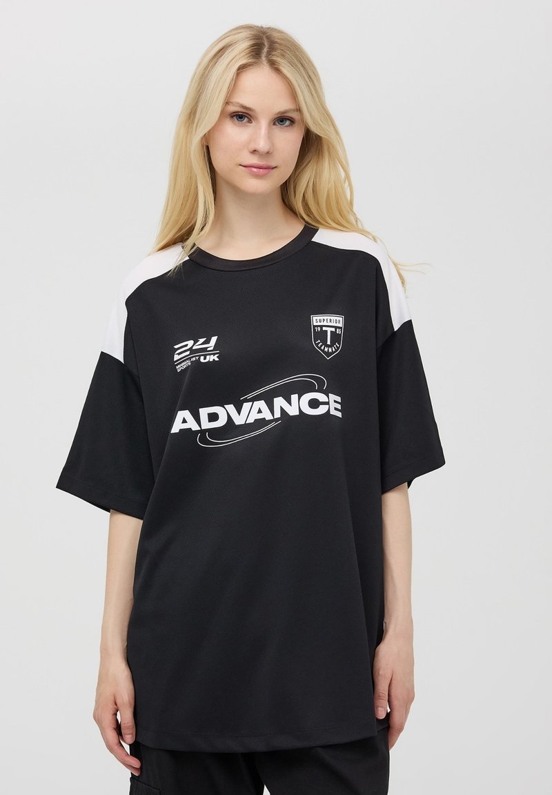 Maglia nera con accenti bianchi, vestibilità ampia, maniche corte, con la scritta "ADVANCE" e un logo sul davanti. Tessuto a rete.