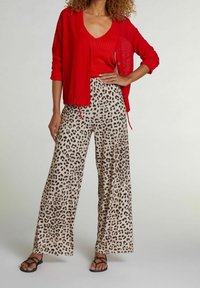 Rød strikket cardigan over en rød top, parret med beige vide bukser med et sort leopardmønster. Sorte sandaler med stropper fuldender looket.