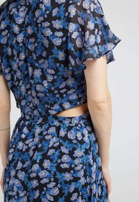 Robe à fleurs avec un fond noir et des motifs de fleurs bleues et jaunes. Comprend un décolleté en découpe et des manches volant.