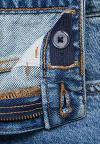 Denim tkanina svijetloplave boje, s žutim šavovima, vidljivim zatvaračem i tamnoplavom oznakom od tkanine sa prozirnim gumbom.