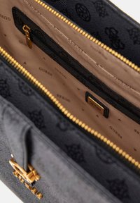 Borsa a tracolla nera in materiale sintetico con dettagli dorati, chiusura con zip e interno beige con motivo a logo del marchio ripetuto.