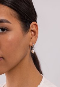 Silberne Creolen mit einem kleinen Perlenanhänger. Der Ring ist mit einer Reihe kleiner Kristalle verziert, die zusätzliche Details bieten.