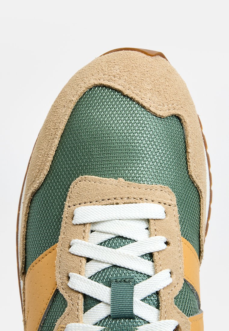 Zapatillas verde y marrón con una parte superior de malla texturizada, detalles en ante, cordones blancos y un distintivo diseño en naranja en el lateral.