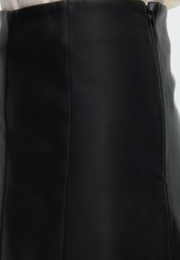 Μαύρη δερμάτινη φούστα με ορατές ραφές και πλευρικό φερμουάρ, φορεμένη με λευκό τοπ.