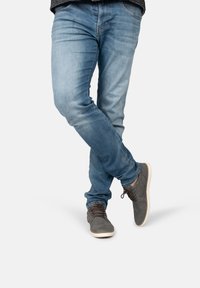 Grijze suède schoenen met witte zolen, gecombineerd met lichtblauwe jeans. De jeans hebben een iets versleten textuur en een slim fit ontwerp.
