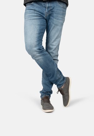 Grijze suède schoenen met witte zolen, gecombineerd met lichtblauwe jeans. De jeans hebben een iets versleten textuur en een slim fit ontwerp.