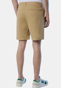 Khaki shorts met een eenvoudig ontwerp, elastische tailleband en achterzak. Draagt een witte sneaker met groene accenten en beige enkellaarzen.