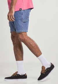 Ljusblå denimshorts med en ficka på vänster sida, bärs med svarta sneakers med bruna detaljer och vita ankelsockor.