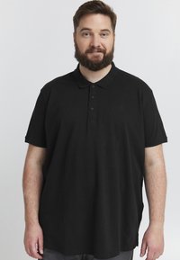 Černé polo tričko s krátkým rukávem, texturovaná tkanina, límeček na knoflíky a jemné logo na levé hrudi. Klasický design.