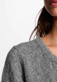 Grauer Wollpullover mit strukturiertem Finish, V-Ausschnitt und weiten, lockeren Ärmeln. Der Stoff wirkt weich und gemütlich.