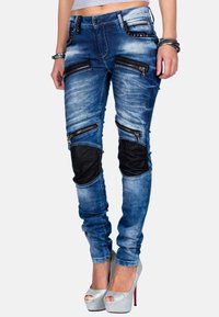 Jeans skinny in denim blue sbiadito con molte tasche con zip e dettagli in pelle nera sulle ginocchia. Presenta un design aderente e una cintura con borchie.