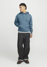Blå hættetrøje lavet af en blanding af bomuld med en kængurulomme, parret med mørk denim jeans, der har en afslappet pasform og oprullede ærmer.