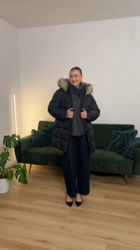 Svart dunjakke med avtakbar hette i kunstpels, glidelåslukking og lommer med knapper, kombinert med en mørk genser og vidbukser.