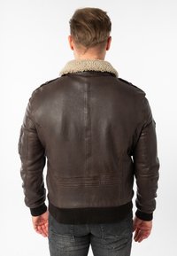 Bruine leren jas met een schapenleren kraag, geribbelde manchetten en zoom. Bevat schouderepauletten en rugnaden voor extra structuur.