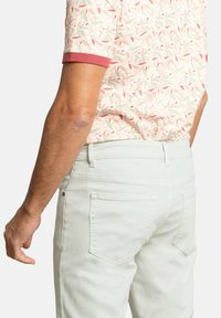 Camisa de manga corta con estampado en suaves tonos pasteles, con un ribete rojo, combinada con pantalones verdes claros que cuentan con bolsillos estándar.