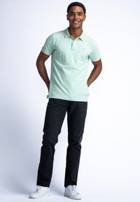 Koszulka polo w miętowym kolorze z czerwonymi akcentami na kołnierzyku i rękawach, połączona z czarnymi dżinsami i białymi trampkami.
