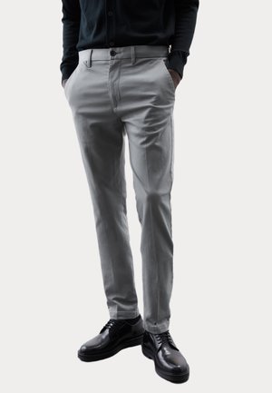 Pantalones ajustados de un gris claro, con bolsillos laterales y trabillas para cinturón, combinados con zapatos de cuero negro, presentando una textura de tela suave.