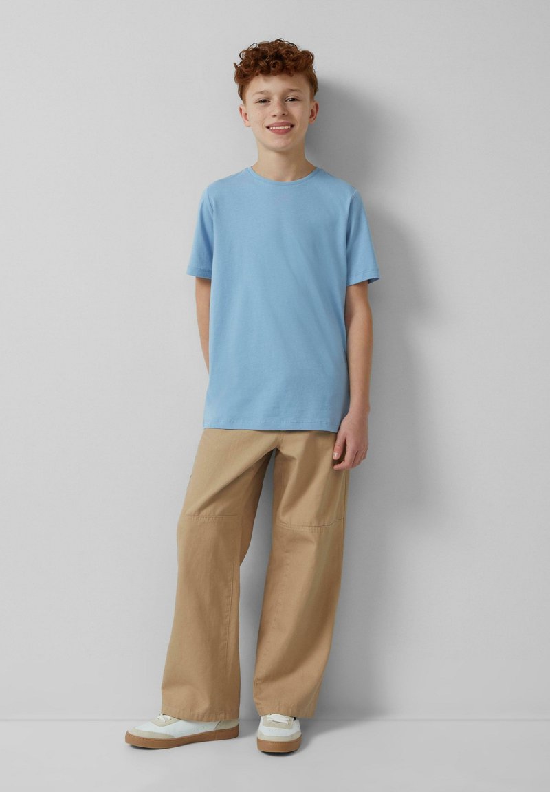 Lichtblauwe katoenen t-shirt met een ronde hals, gecombineerd met beige wijde broek en witte sneakers met tan accenten. Eenvoudig ontwerp, casual pasvorm.