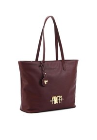 Borsa a tracolla in pelle bordeaux con hardware dorato, caratterizzata da un charm rotondo e un testo impresso "YNOT?" sul fronte. Texture liscia e forma strutturata.