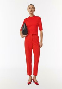 Red knit top with short sleeves, high-waisted red trousers, black handbag, and red high-heeled shoes. Simple design, smooth texture.