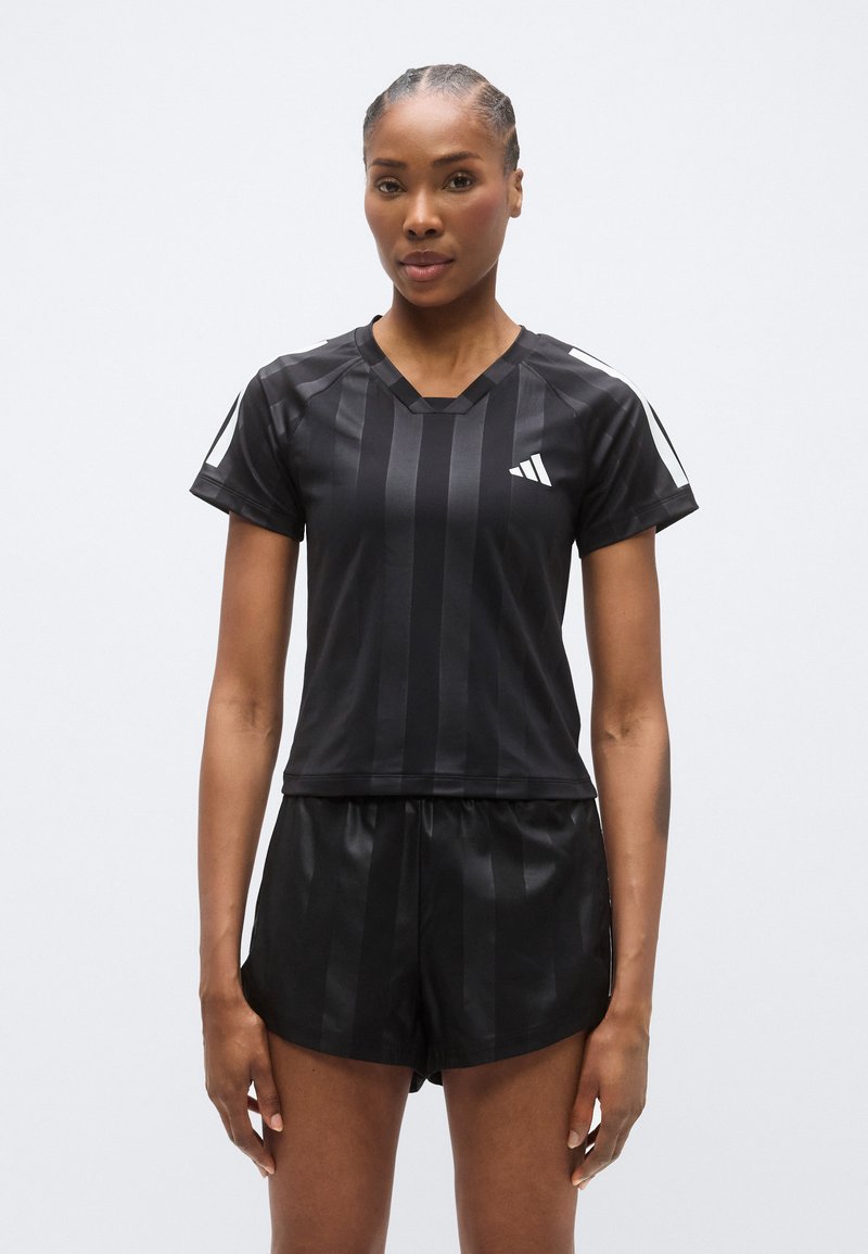 Tenue de sport noire comprenant un haut ajusté à manches courtes avec des rayures verticales et un short assorti, tous deux fabriqués dans un matériau lisse et léger.