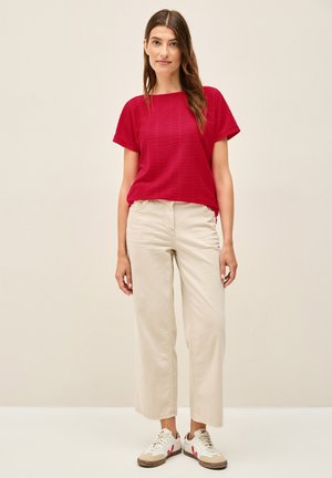 Haut court à manches courtes texturé rouge, accompagné d'un pantalon large beige clair et de baskets blanches avec des accents rouges. Tenue simple et décontractée.