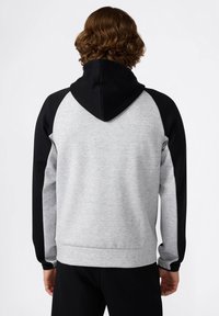 Grauer und schwarzer Kapuzenpullover mit weichem Material, Raglanärmeln und Kordelzug. Die Rückseite zeigt einen Farbblock mit kontrastierenden Farben.