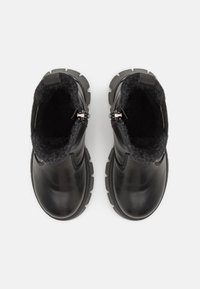 Botas de tobillo de cuero negro con un forro de fieltro suave, diseñadas con una suela robusta y cierre de cremallera. Presentan un upper texturizado y un tacón resistente.