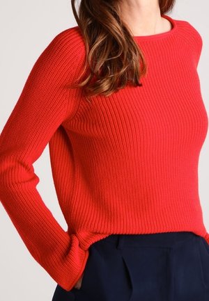 Pull en maille côtelée rouge avec encolure ronde et manches longues, présentant une coupe décontractée et des fentes latérales à l'ourlet.