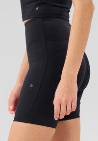 Pantalones cortos negros de talle alto fabricados con una tela elástica. Las características incluyen una textura suave, costuras planas y un pequeño logo en el lateral.