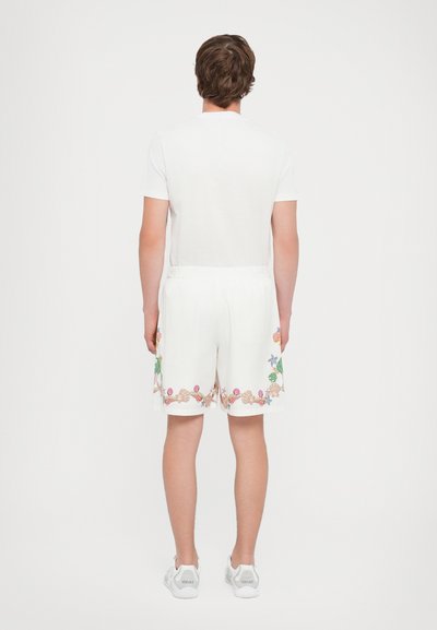 White short-sleeve t-shirt paired with white shorts featuring colorful shell and floral embroidery along the hem. White sneakers complete the look.