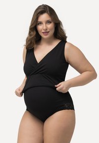 Czarny kombinezon ciążowy z dekoltem w serek, marszczonym detalem w talii i koronkowymi wykończeniami na nogawkach. Gładki, elastyczny materiał.