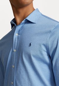 Jasnoniebieska koszula na guziki o miękkiej fakturze, z klasycznym kołnierzykiem i małym haftowanym logo na lewej piersi.