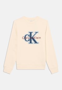 Sudadera de color crema hecha de tejido suave, que presenta un gran logotipo bordado en azul y burdeos con el texto "Calvin Klein" debajo.