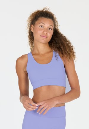 Lichtpaarse sportbeha met een ronde halslijn en brede bandjes. Glad, rekbaar materiaal met een brede band aan de onderkant, geschikt voor sportkleding.