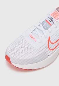 Nike Interact Run tenisice imaju prozračnu bijelu mrežicu na gornjem dijelu, narančaste akcentne detalje, debeli potplat i QR kod oznaku na jeziku.